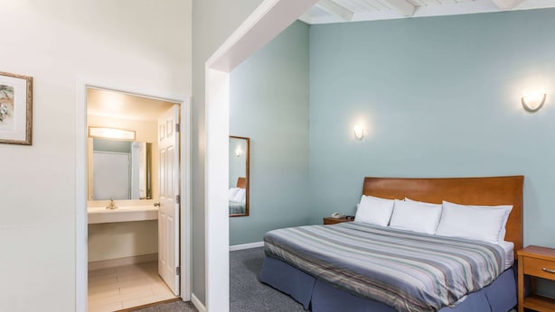 A bedroom with a bed, a nightstand, a bedside table, a mirror, and a door leading to a bathroom.