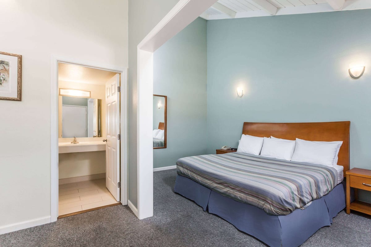 A bedroom with a bed, a nightstand, a bedside table, a mirror, and a door leading to a bathroom.