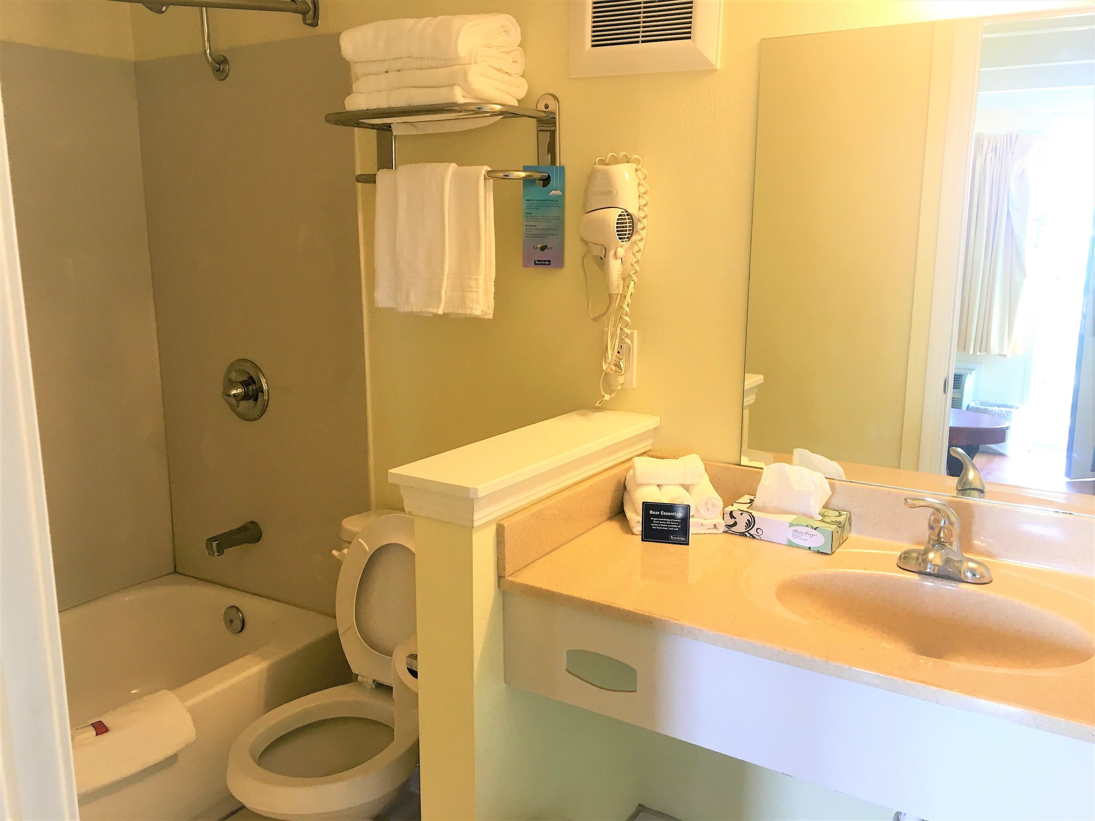Un baño con inodoro, lavamanos, espejo, toallero y secador de pelo.