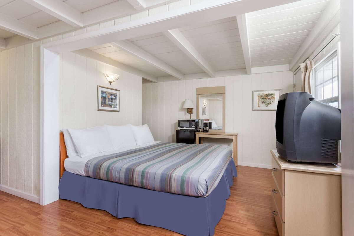 A bedroom with a bed, a desk with a microwave, a television, and a dresser.