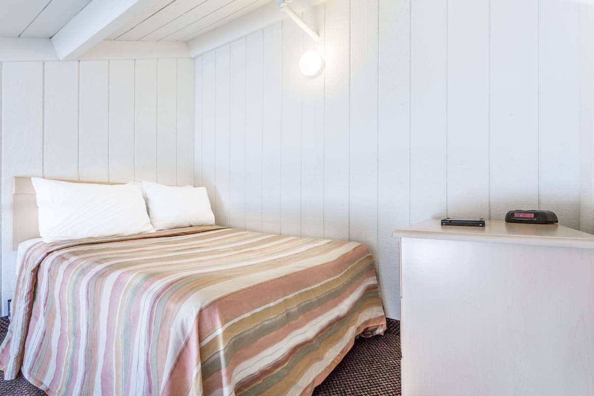 A hotel room with a bed, a bedside table, and a wall-mounted light.