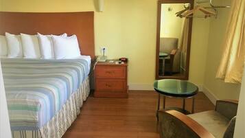 Een hotelkamer met een bed, nachtkastje met telefoon, spiegel, stoel en kapstok.