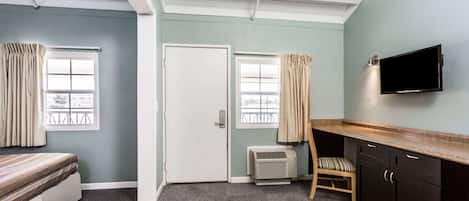 A room with a bed, a desk, a chair, a television, and a door.