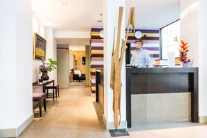 A reception area with a modern design, featuring a reception desk, a clock, and a potted plant. - Hotel Duret (Paris)
