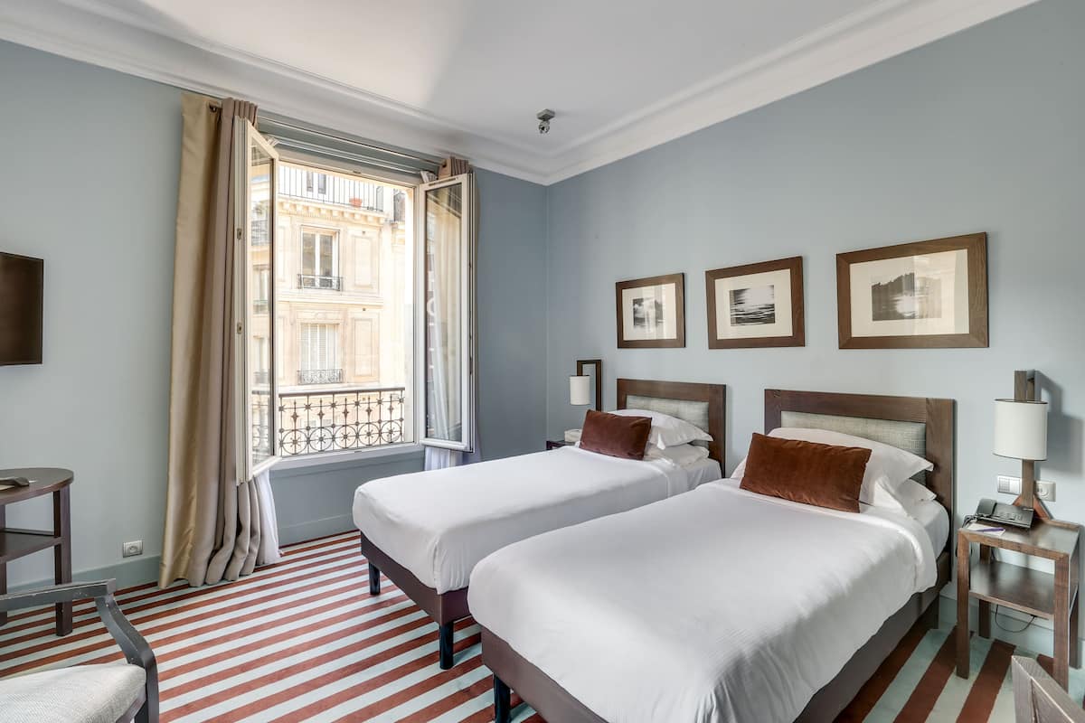 Una habitación de hotel con dos camas, una ventana con cortinas, un suelo a rayas y cuadros en la pared.
