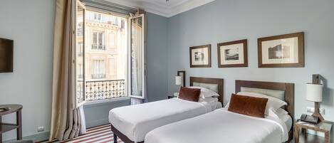 A hotel room with two beds, a window with curtains, a striped floor, and framed pictures on the wall.