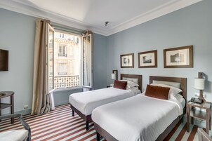 Una habitación de hotel con dos camas, una ventana con cortinas, un suelo a rayas y cuadros en la pared.