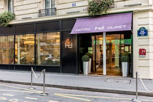 Entrada de un hotel con un toldo morado, puertas de vidrio y un letrero visible que dice 'Hotel Duret'.