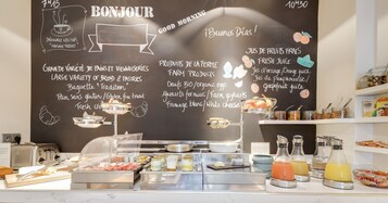 Zona de bufé para desayuno con un menú en pizarra que ofrece pan, bollería, productos de la granja y zumo fresco.