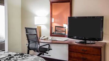 Et hotelværelse med seng, skrivebord med stol, fladskærms-tv, et spejl, en lampe og en telefon.