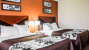 A hotel room with two beds, a nightstand with a lamp, and framed pictures on the wall.