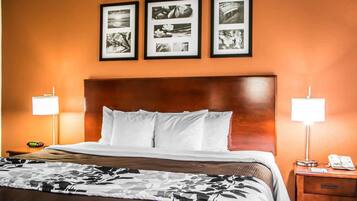 A hotel room with a large bed, two bedside lamps, a nightstand with a phone, and three framed pictures on the wall.