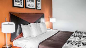 Une chambre d’hôtel avec un grand lit, deux tables de chevet, une lampe fixée au mur et des tableaux encadrés au-dessus du lit.