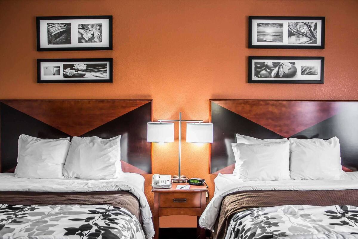 Ein Hotelzimmer mit zwei Betten, einem Nachttisch mit Lampe und gerahmten Bildern an der Wand.