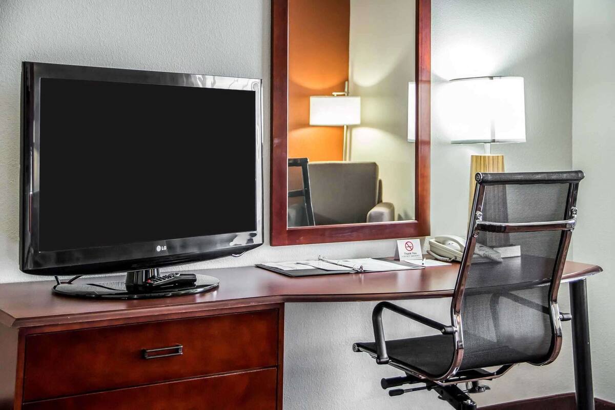 Ein Hotelzimmer mit einem großen Flachbildfernseher, einem Holztisch, einem Stuhl, einer Lampe und einem Telefon.