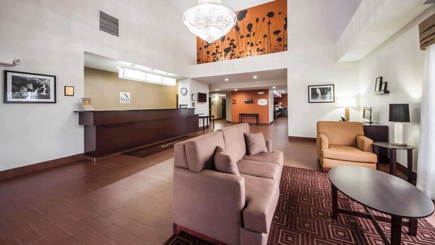 A hotel lobby with a reception desk, a sofa, a chair, and a chandelier.
