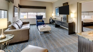 A hotel room with a sofa, a blue armchair, a desk with a computer, a TV, and a bed.