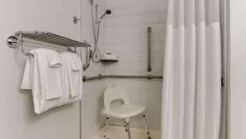 Ein Badezimmer mit Duschstuhl, Haltegriffen und Handtuchhalter.