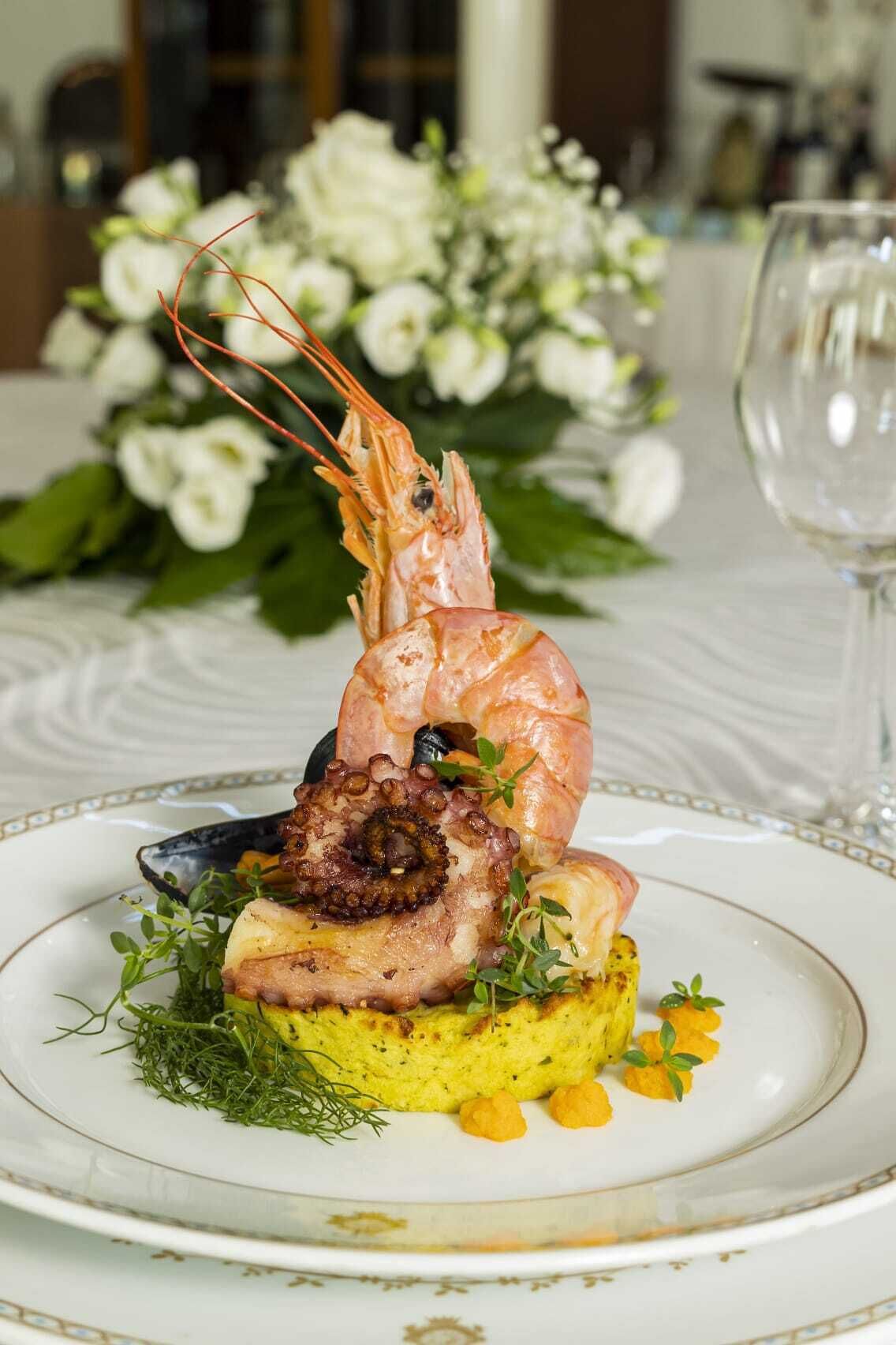 A seafood dish with shrimp, octopus, and mussels on a bed of potatoes, garnished with herbs, served on a white plate.