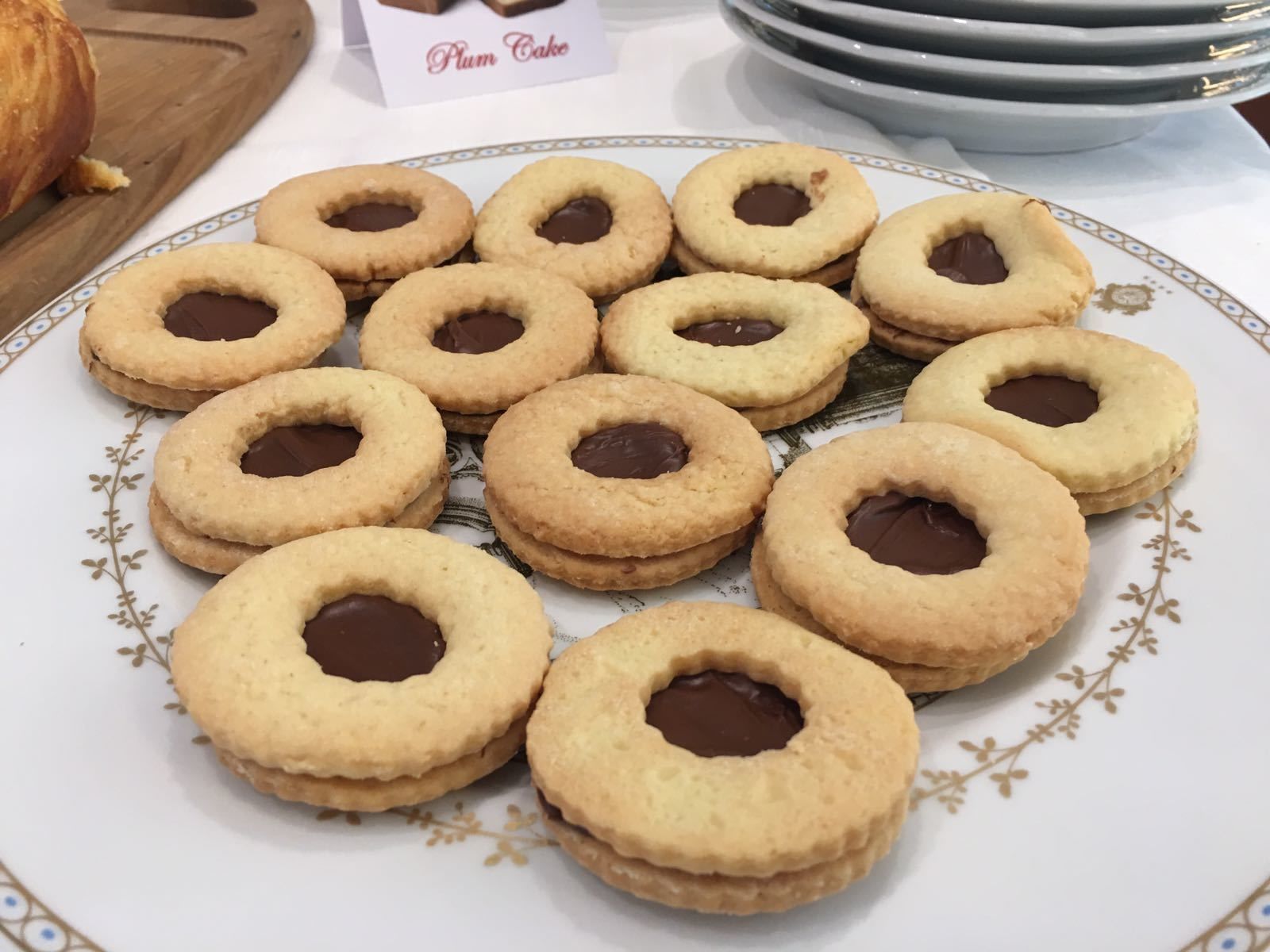 En tallrik med runda kakor med chokladfyllning, en skylt med texten ”Plommonkaka” och en hög med tallrikar i bakgrunden.