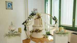 Een drielaagse bruidstaart met witte frosting en gouden accenten, omringd door groen en witte bloemen.