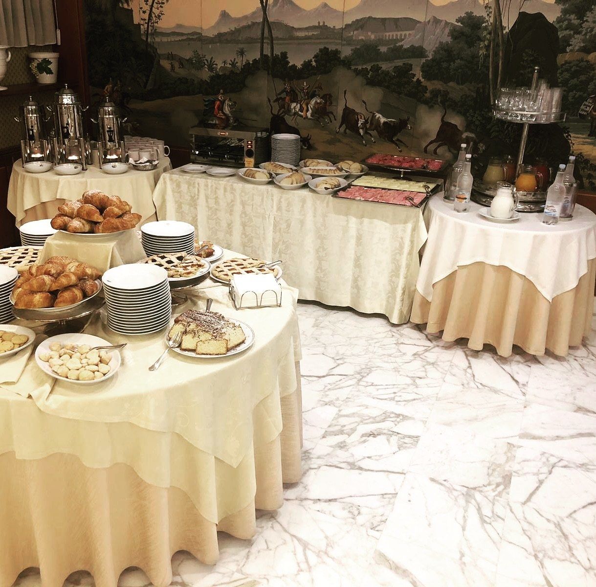 A buffet setup with various food items and beverages on tables, set against a mural backdrop.