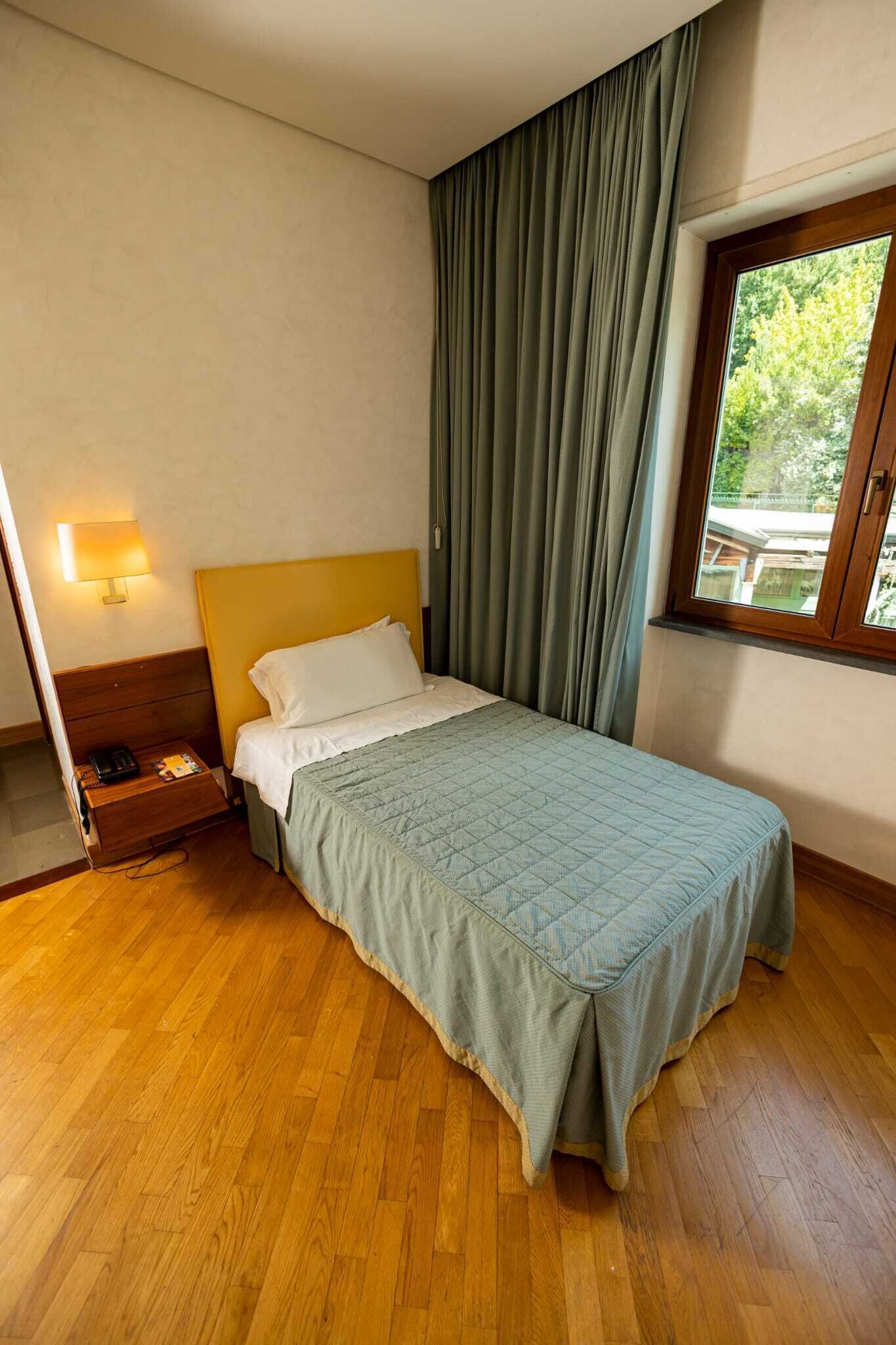 Ein Einzelbett mit gesteppter Bettdecke, eine Nachttischlampe und ein Nachttisch aus Holz mit einem Telefon.