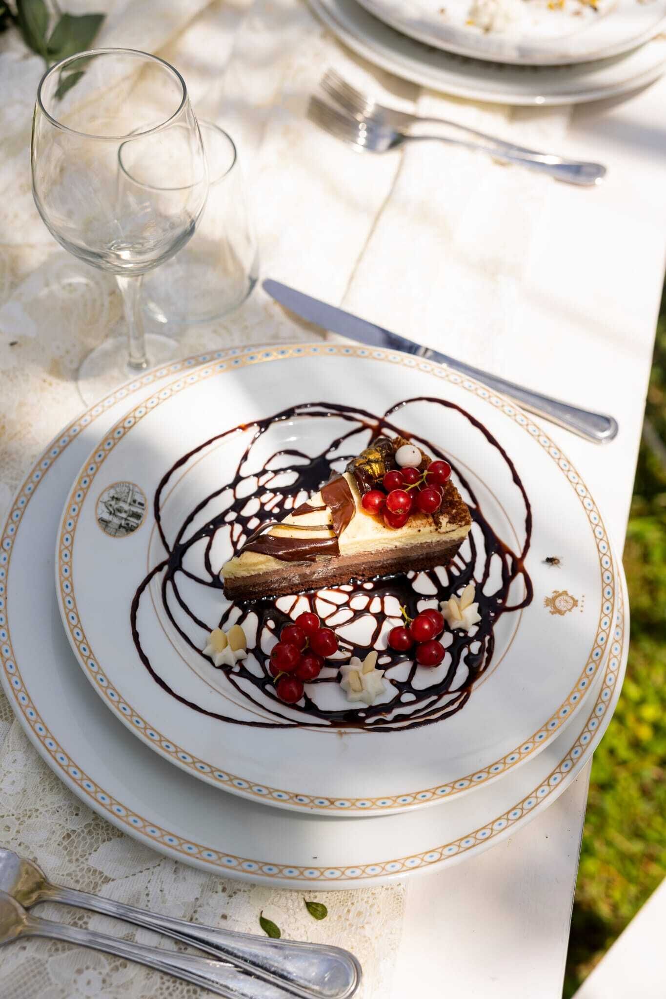 Un dessert servi dans une assiette blanche à bord doré, accompagné d’une fourchette et d’un verre à vin, le tout posé sur une table.