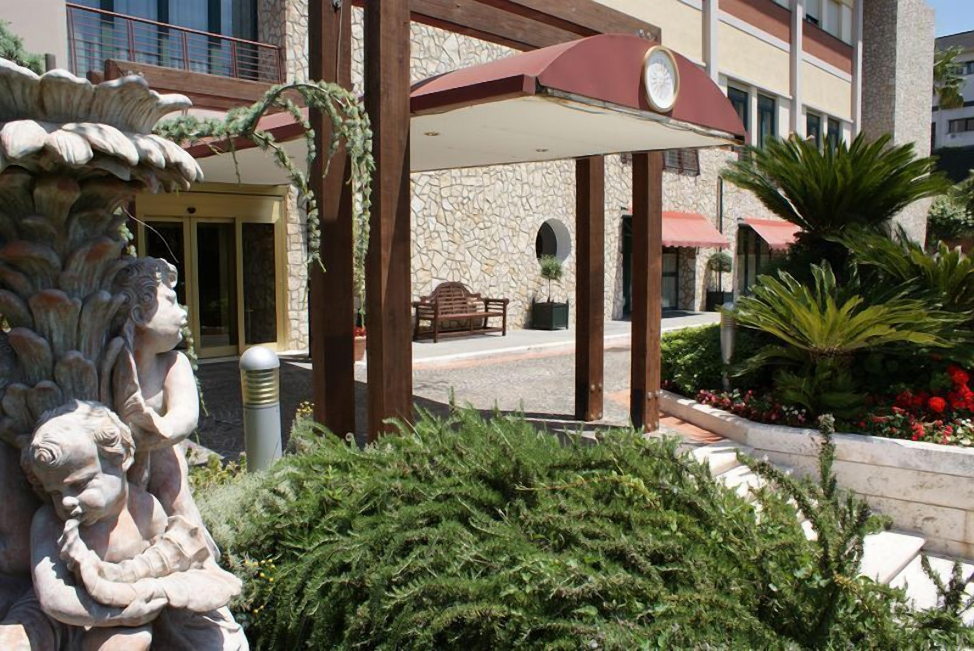 A stone building with a covered entrance, outdoor seating, and a statue of cherubs.