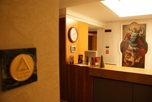A reception desk with a clock, framed certificates, and a painting on the wall.
