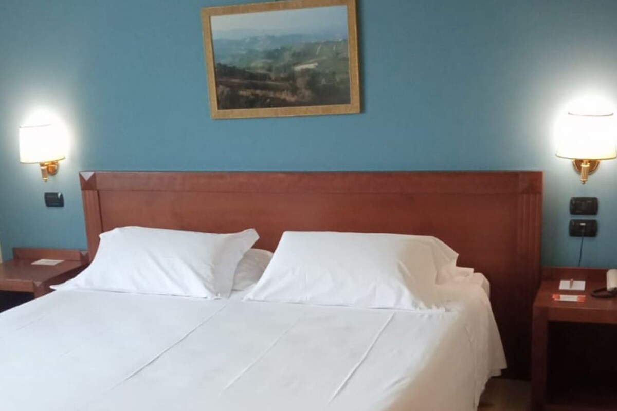 A neatly made bed with white linens, a wooden headboard, and two bedside lamps.