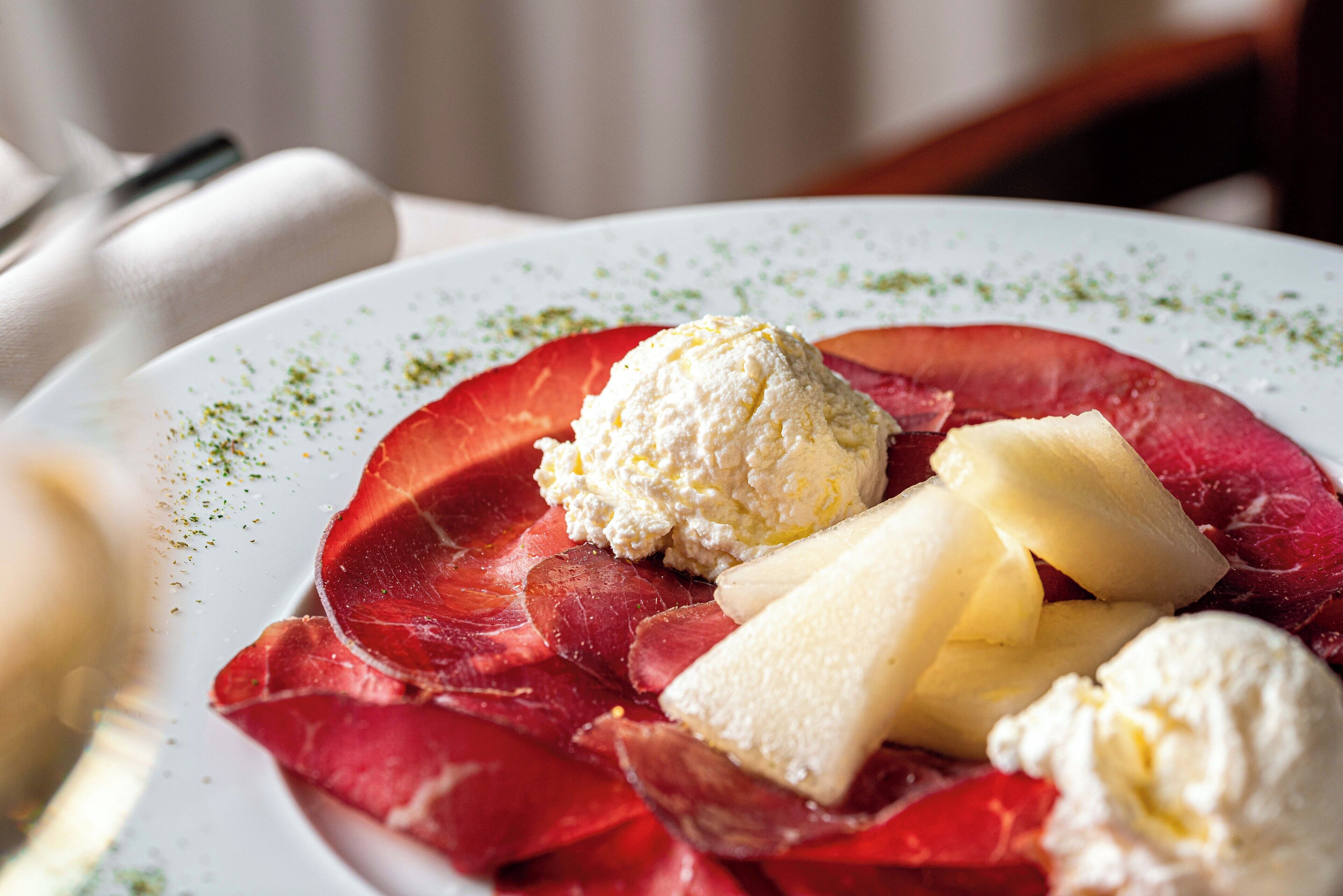 A plate with slices of cured meat, cheese, and a scoop of ice cream.