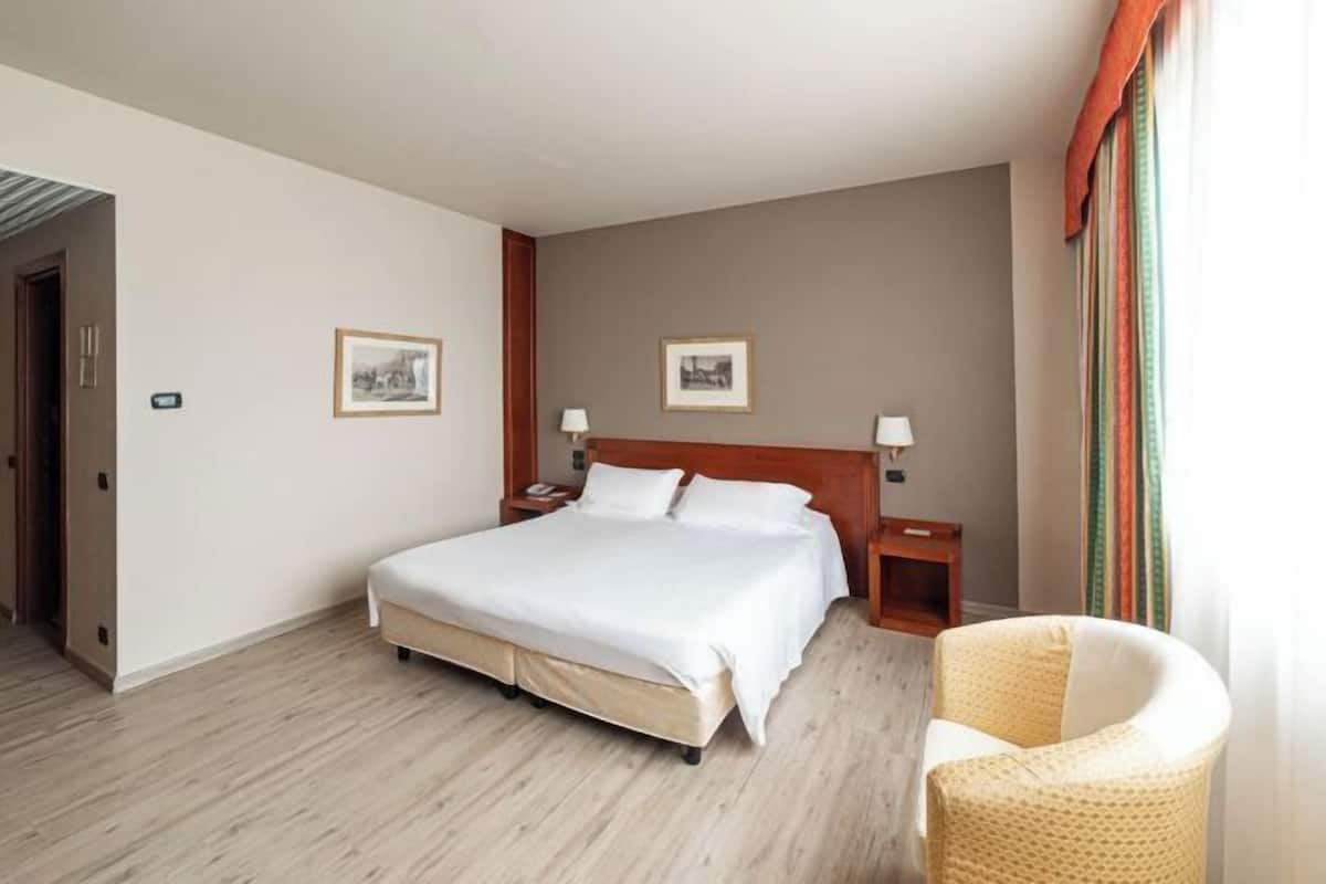 Une chambre d’hôtel avec un lit, des tables de chevet, une chaise et deux tableaux encadrés au mur.