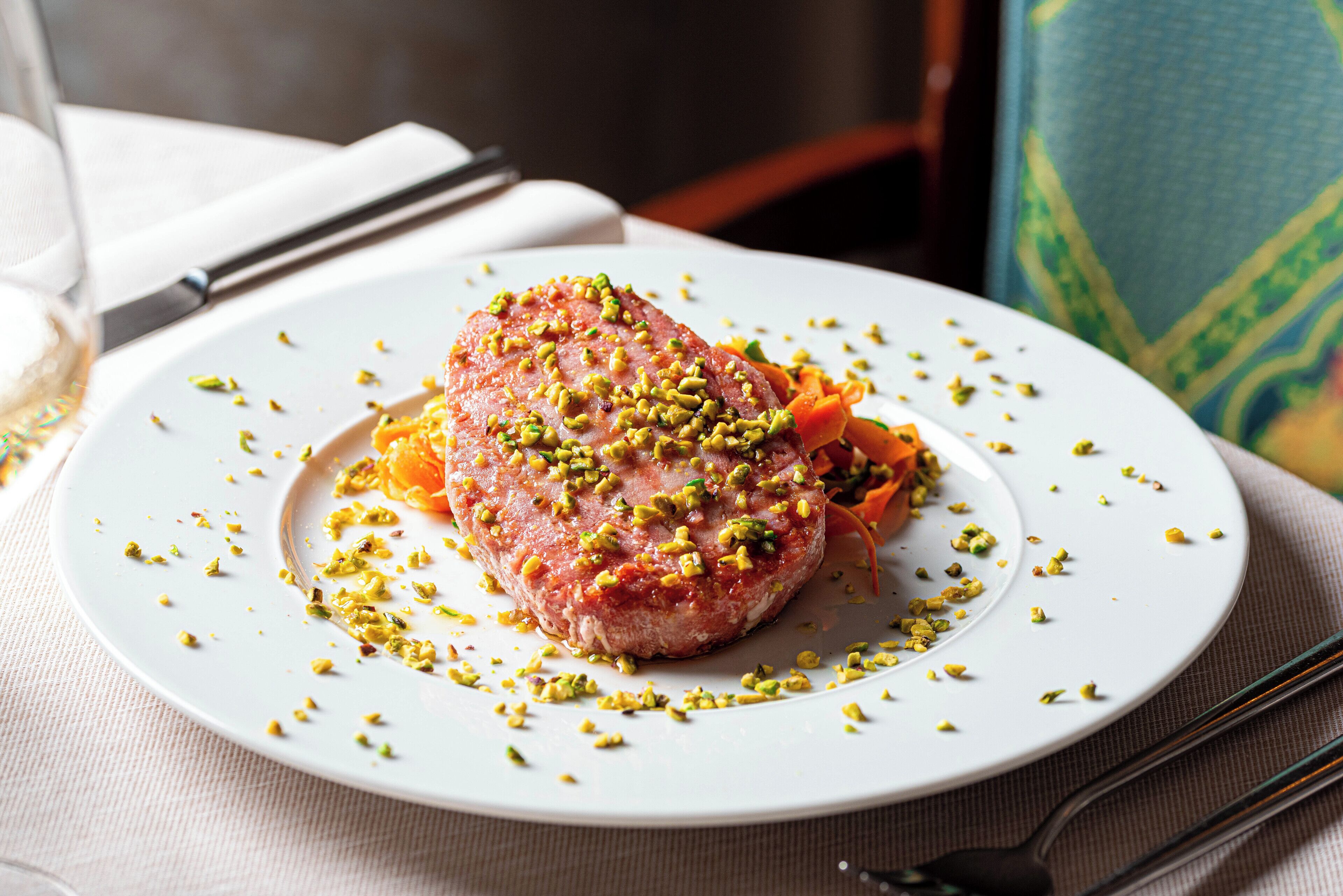 Un plato blanco con un guiso de carne adornado con hierbas verdes, sobre una mesa con mantel blanco.