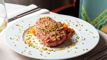 Un plato blanco con un guiso de carne adornado con hierbas verdes, sobre una mesa con mantel blanco.