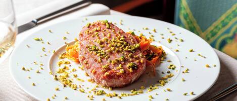 Un plato blanco con un guiso de carne adornado con hierbas verdes, sobre una mesa con mantel blanco.