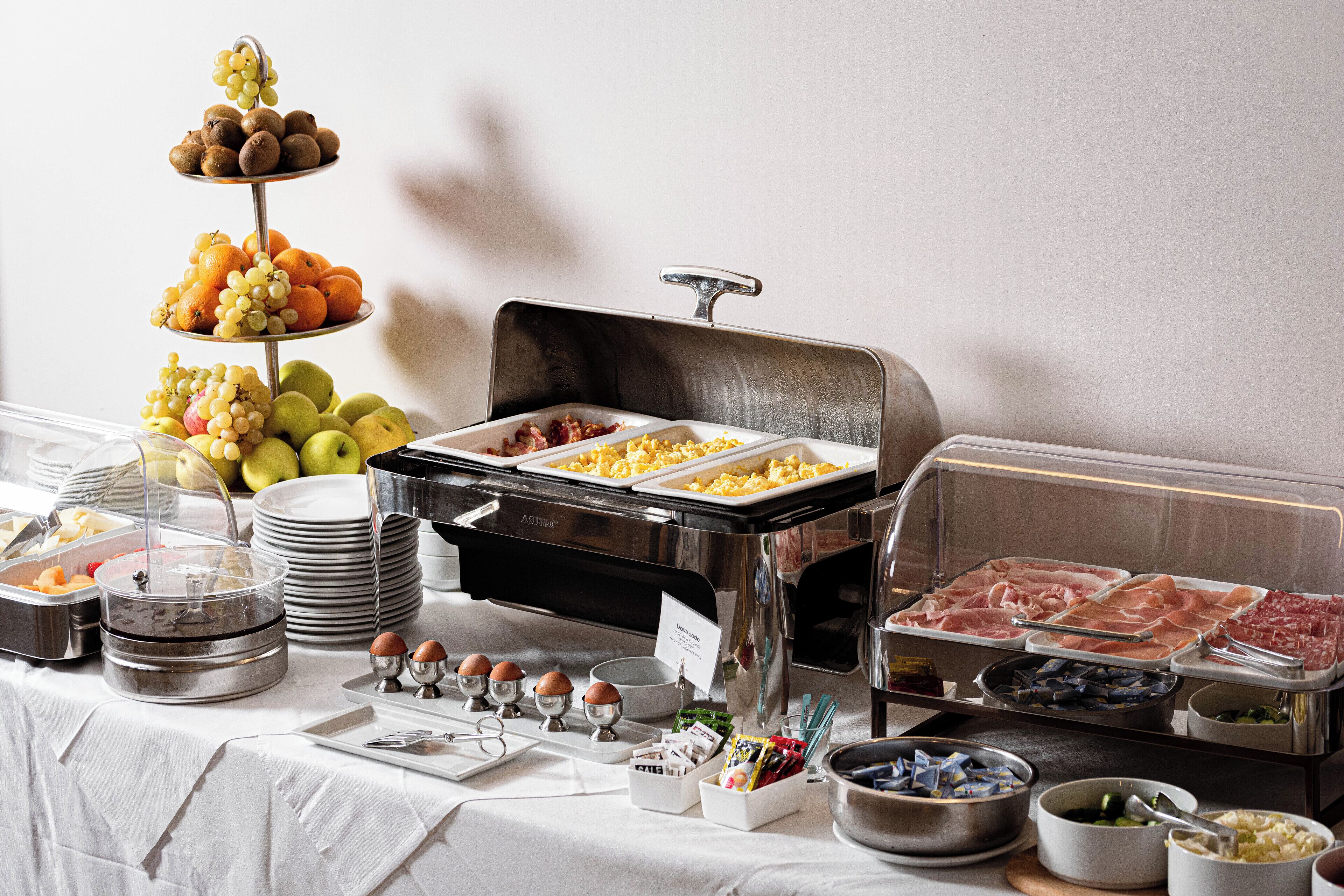 A buffet setup with various food items, including fruits, eggs, and meats.
