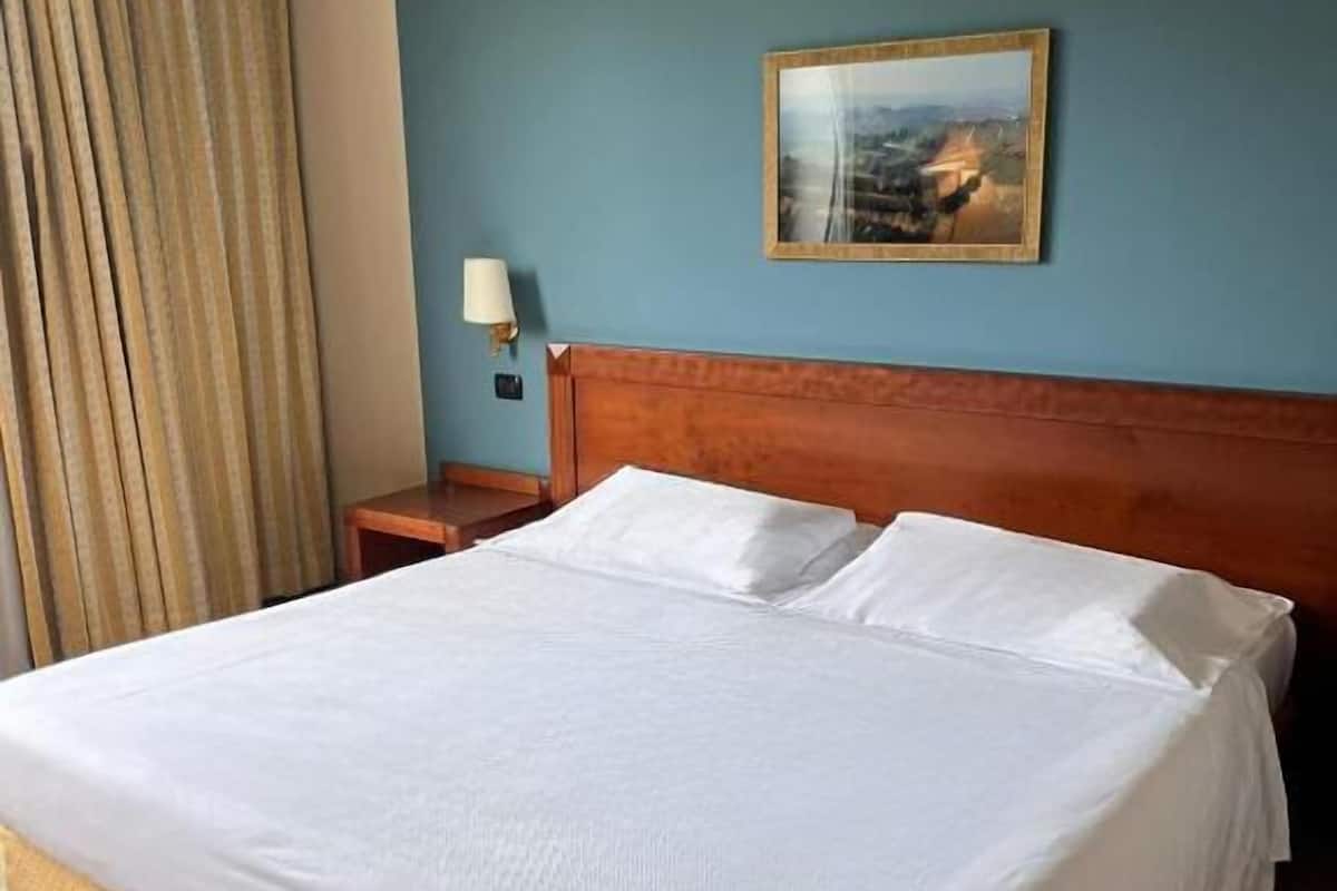 Une chambre d’hôtel avec un grand lit, une tête de lit en bois, une table de chevet avec une lampe et un tableau au mur.