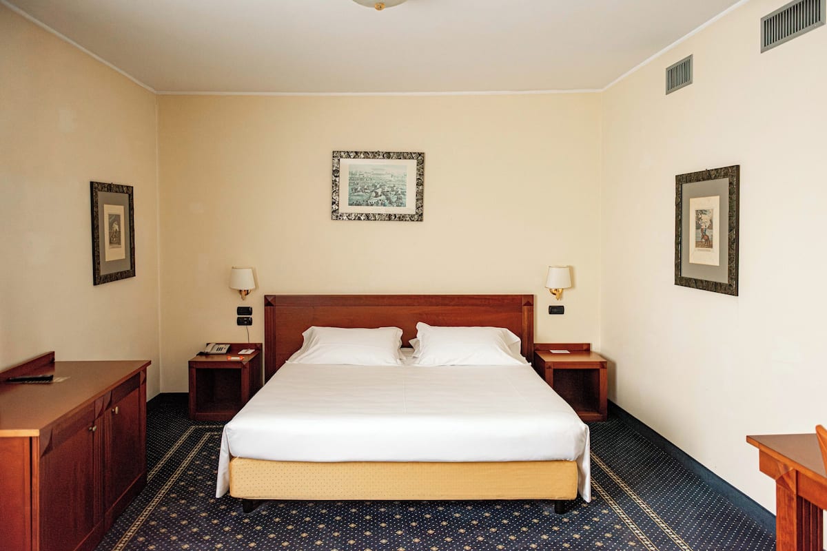 Une chambre d’hôtel avec un grand lit, deux tables de chevet, une commode en bois et un ventilateur de plafond.