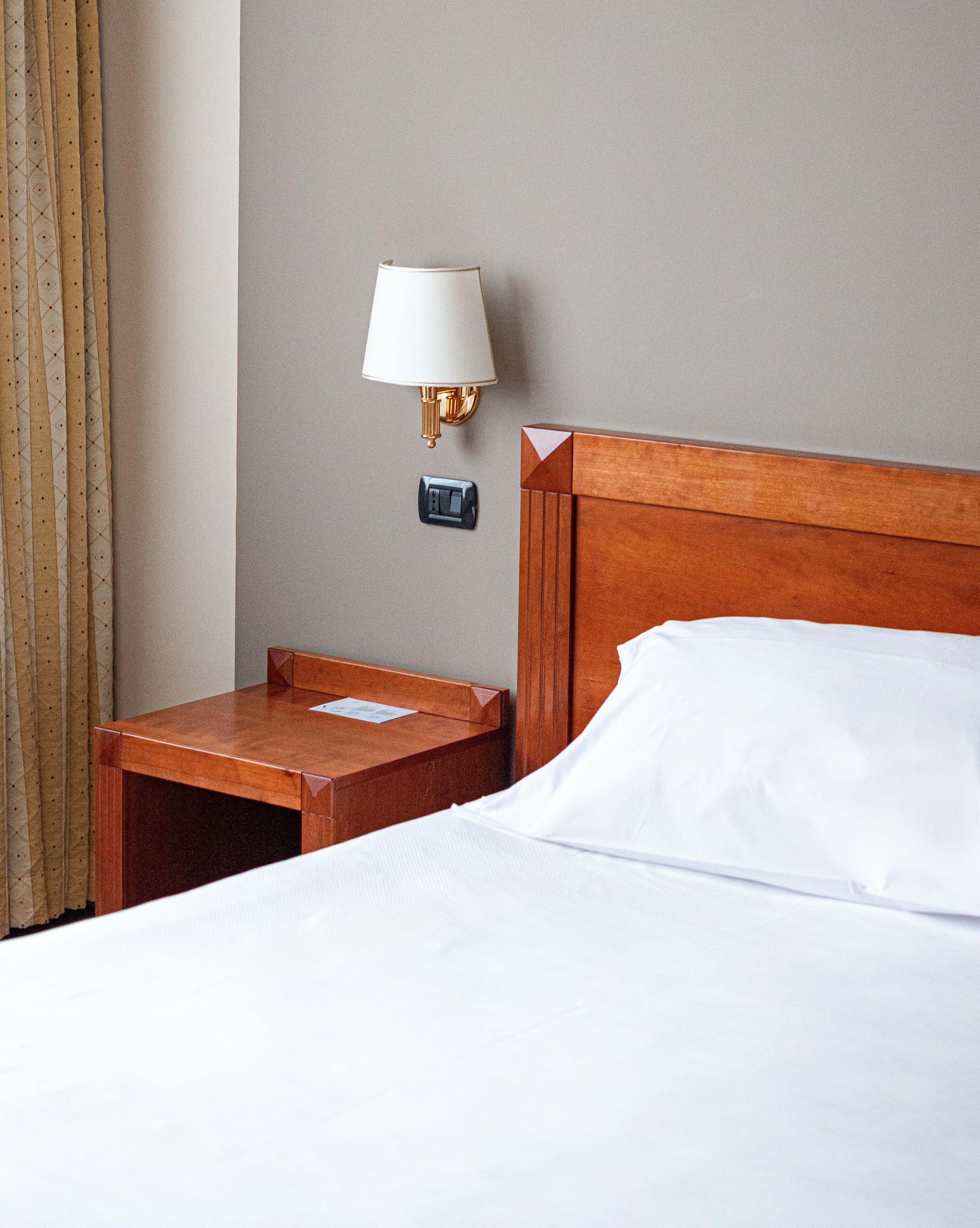 Ein Hotelzimmer mit einem hölzernen Kopfteil, einem Nachttisch mit Lampe und einer Steckdose.