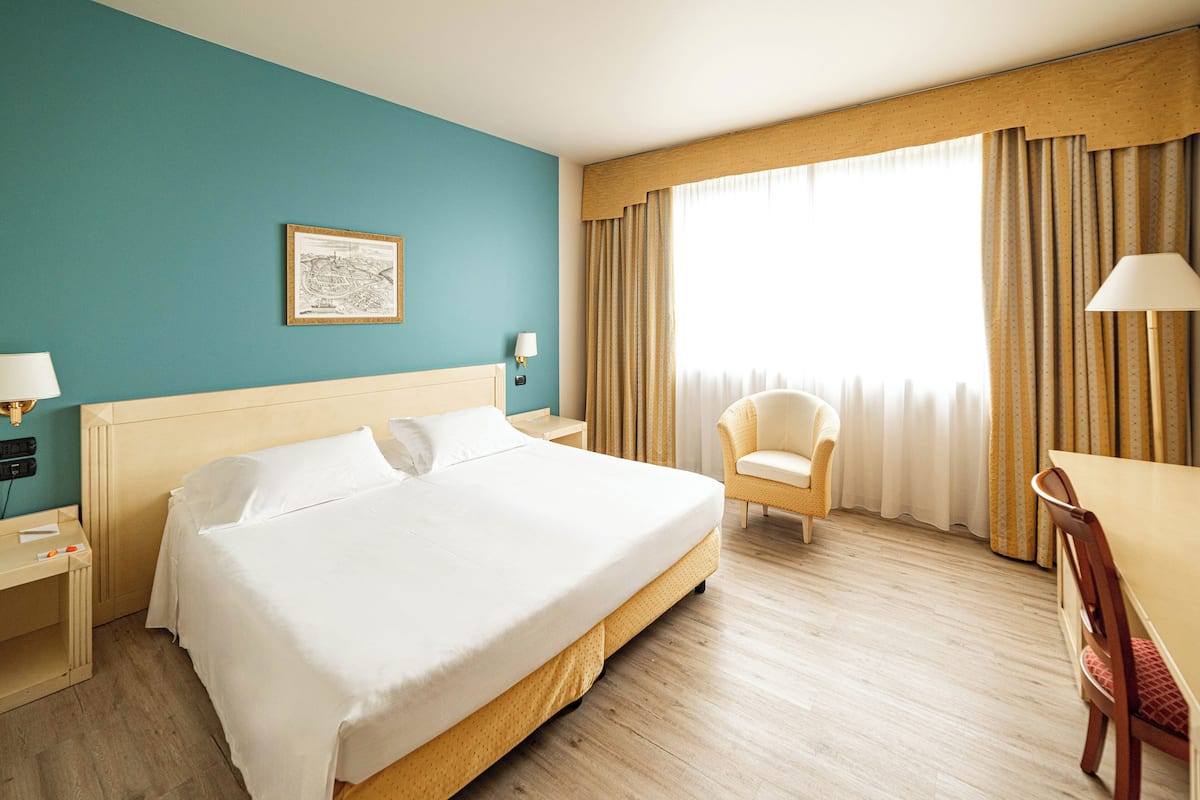 Une chambre d’hôtel avec un grand lit, une chaise, un bureau et une fenêtre avec des rideaux.