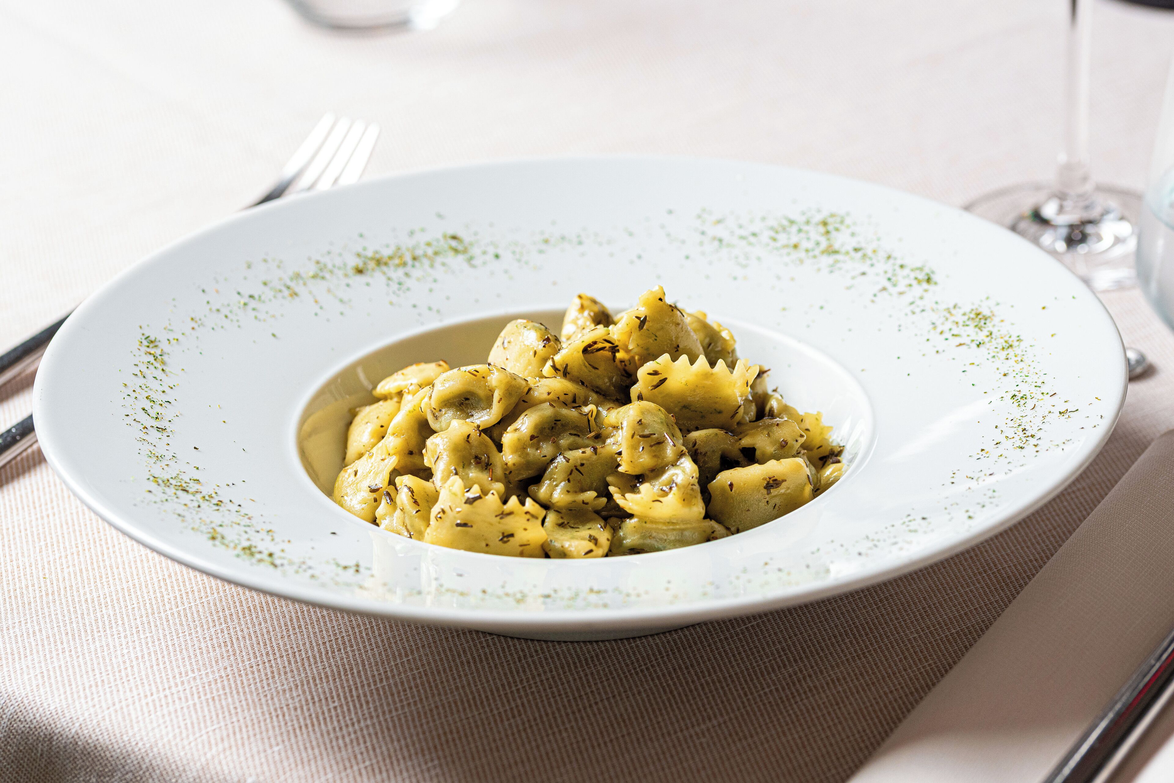 Un plato de pasta con salsa cremosa, adornado con hierbas, sobre un plato blanco con borde moteado.