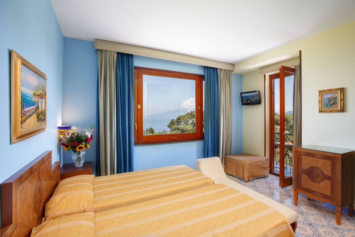 Een hotelkamer met een bed, een klein tafeltje, een televisie en een balkon met uitzicht.