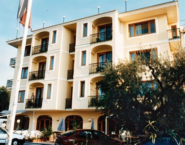 Un hôtel à plusieurs étages, doté de balcons, avec une voiture garée devant et des plantes en pot.