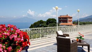 Une terrasse dotée de meubles en osier, d’une balustrade et offrant une vue sur la mer et les montagnes.