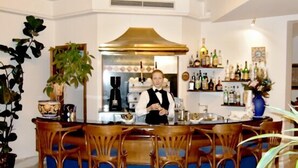 Un espace bar avec un barman, des chaises en bois, un comptoir avec des bouteilles et une plante décorative.