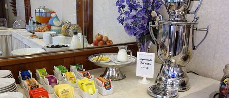 A buffet setup with various food items, a coffee station, and a sign indicating hot water availability.