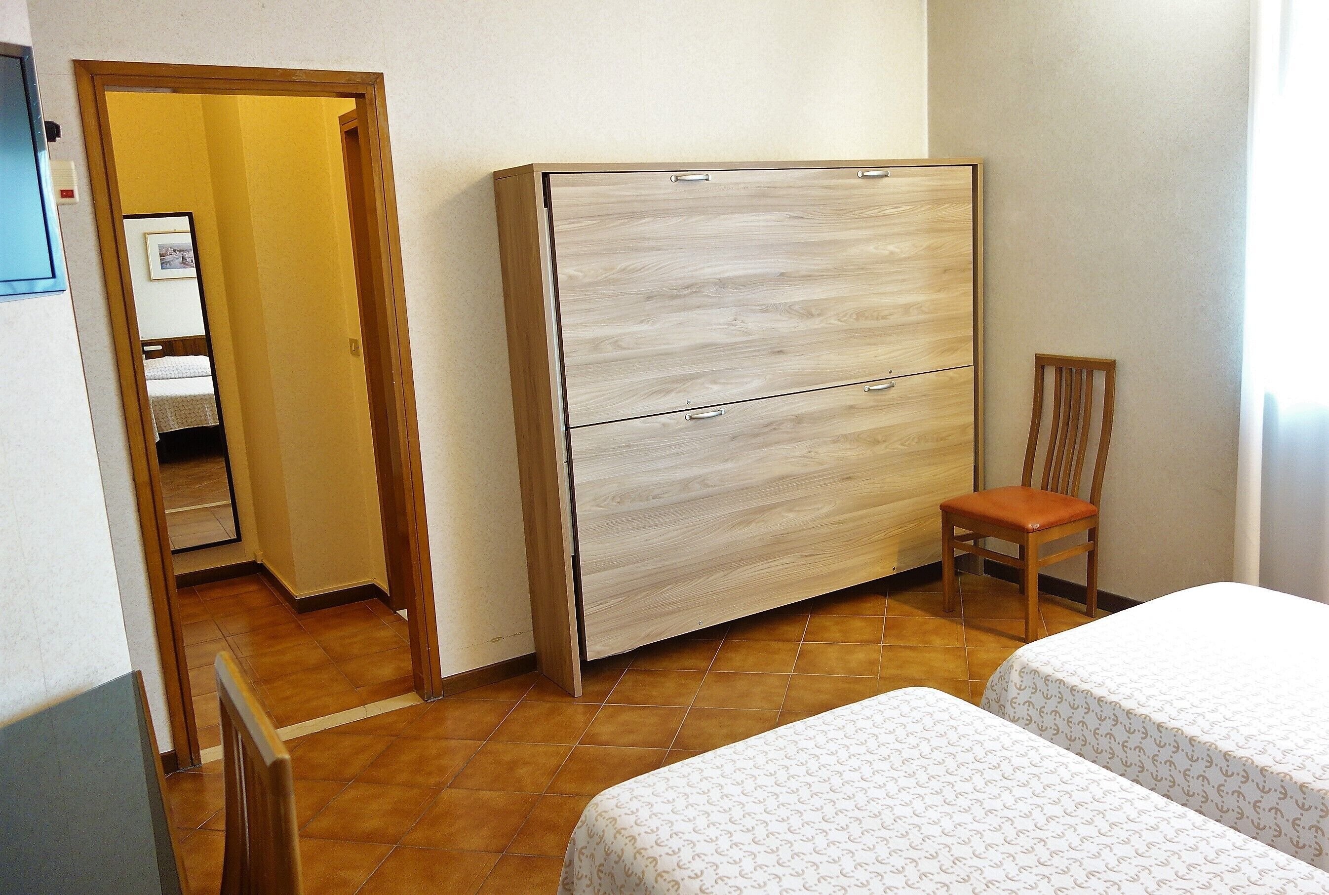 Camera da letto con un'armadio in legno, una sedia e due letti con copriletto decorato.