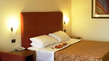 Una habitación de hotel con una cama, una mesita de noche con teléfono, una silla roja y un otoman blanco.