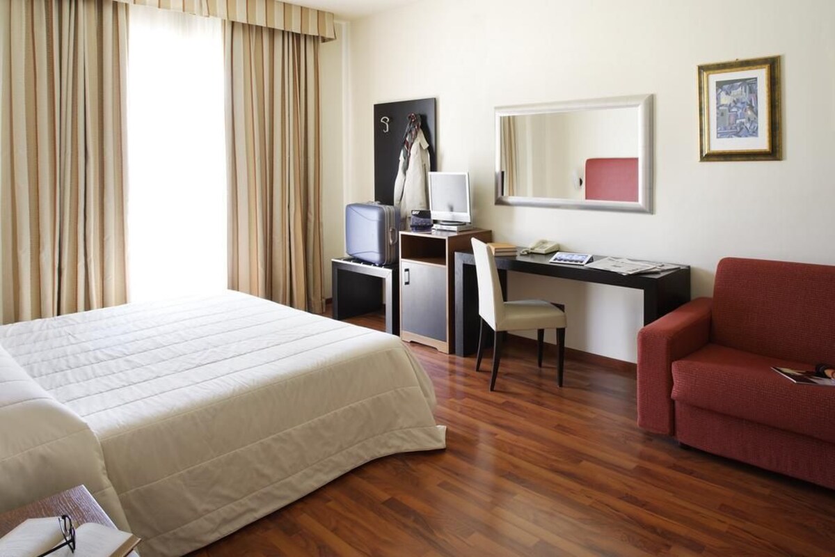 A hotel room with a bed, a desk with a computer, a chair, and a red sofa.